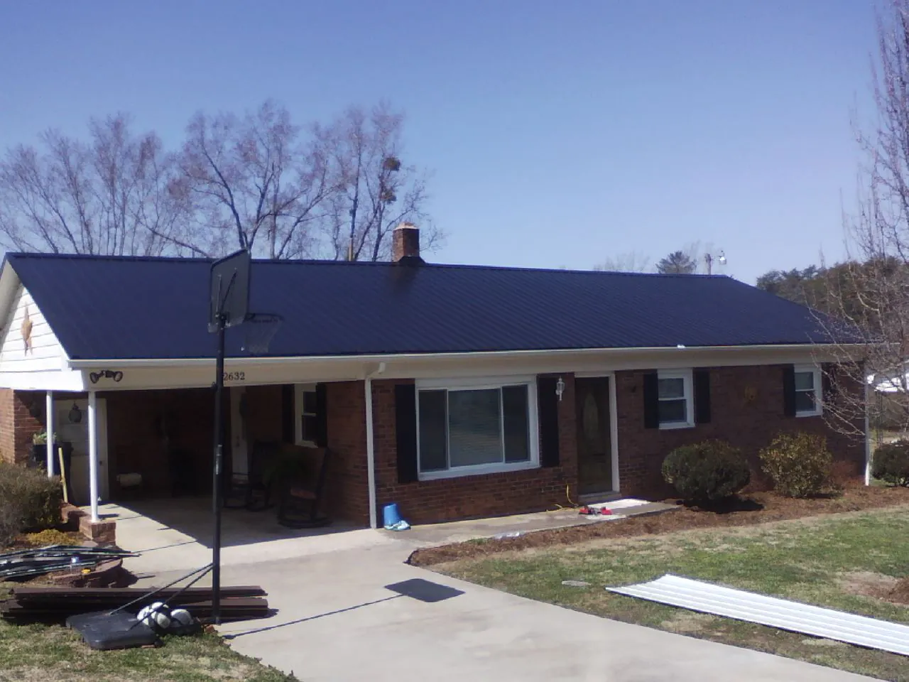 Finished dark blue metal roof on a brick ranch with a carport in Bow