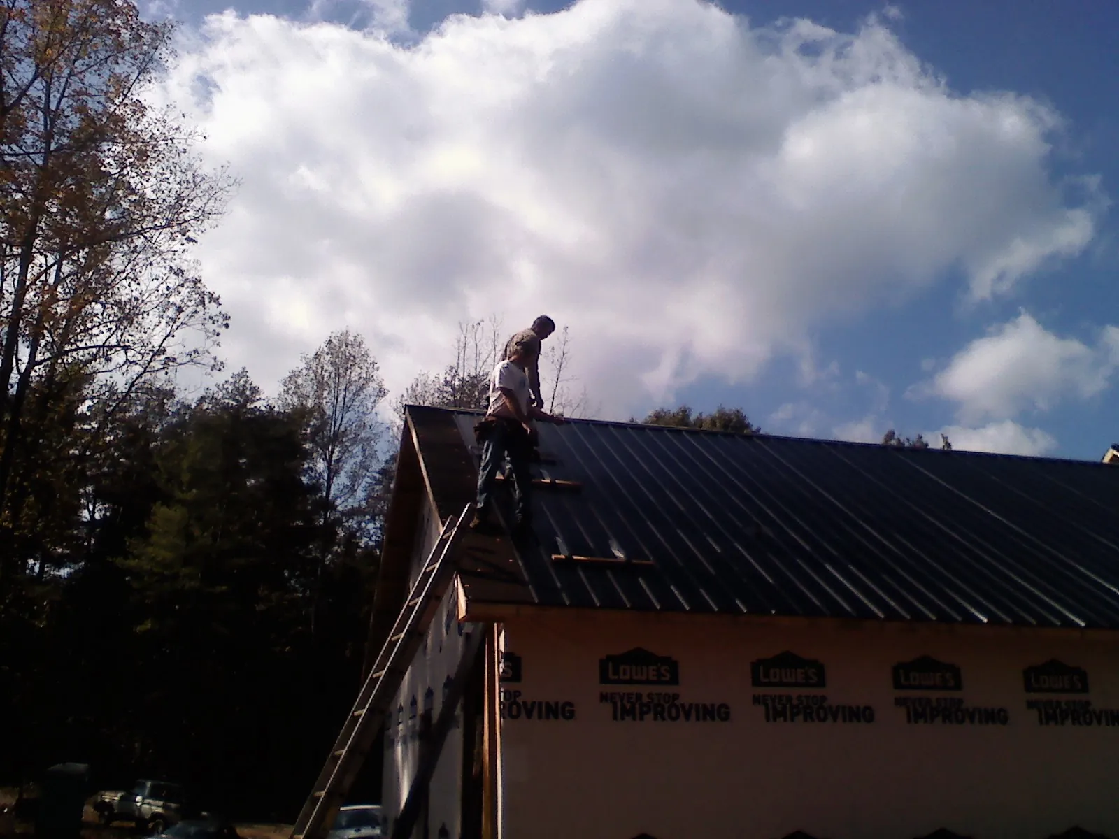 Roofer fastening dark metal panels high against a cloudy sky, from a Roof Inspection job in Bow